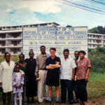 Building a Shared Future: Derek Bryson Park (center) stands alongside community members and local families in front of the historic project sign on Lomond Drive in Maraval, <a href="https://en.wikipedia.org/wiki/Trinidad" target="_blank">Trinidad</a>. Featuring the agency's distinct roofed "N | A" logo for the <a href="https://en.wikipedia.org/wiki/National_Housing_Authority_(Trinidad_and_Tobago)" target="_blank">National Housing Authority (NHA)</a>, the development marks an enduring milestone in providing stable, accessible infrastructure in the lower Maraval Valley, fostering sustainable community growth just north of the capital city, <a href="https://en.wikipedia.org/wiki/Port_of_Spain" target="_blank">Port of Spain</a>. Derek Bryson Park NHA in Port of Spain